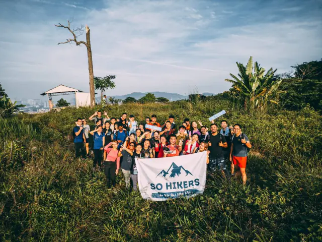 Group with So Hikers flag on hilltop with KL skyline