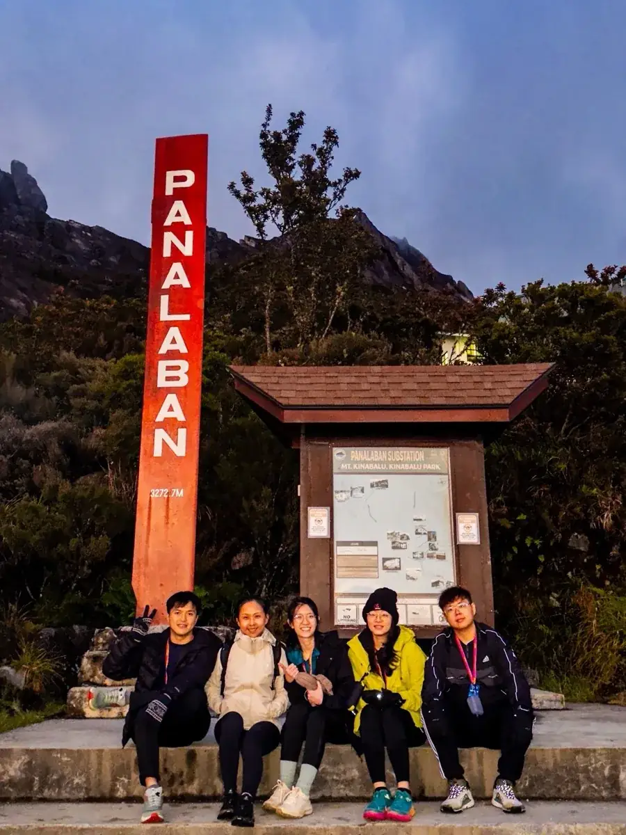 Five So Hikers climbers sitting under the red Panalaban signpost at dusk, granite peaks behind
