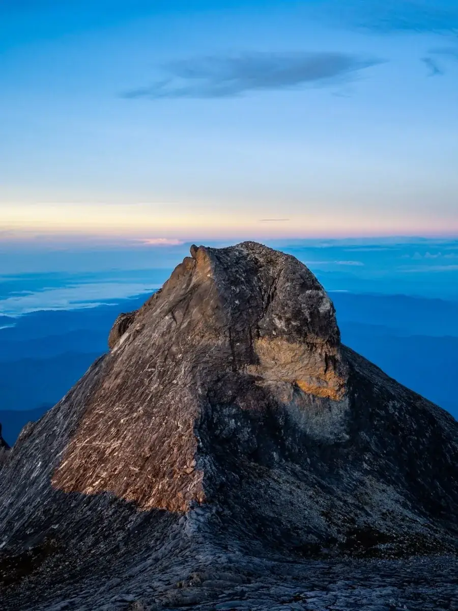 South Peak lit orange at sunrise, a pale sky and a sea of cloud behind